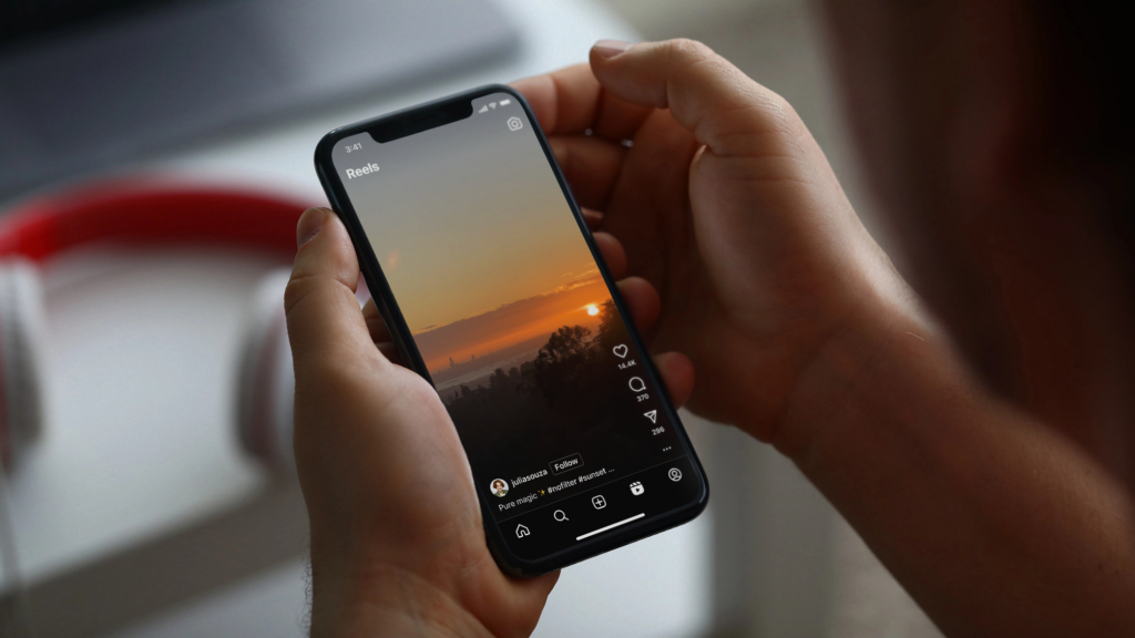 Person holding a smartphone with Instagram Reels open, displaying a sunset scene.